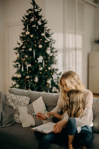 woman with daughter sitting on couch in front of christmas tree
